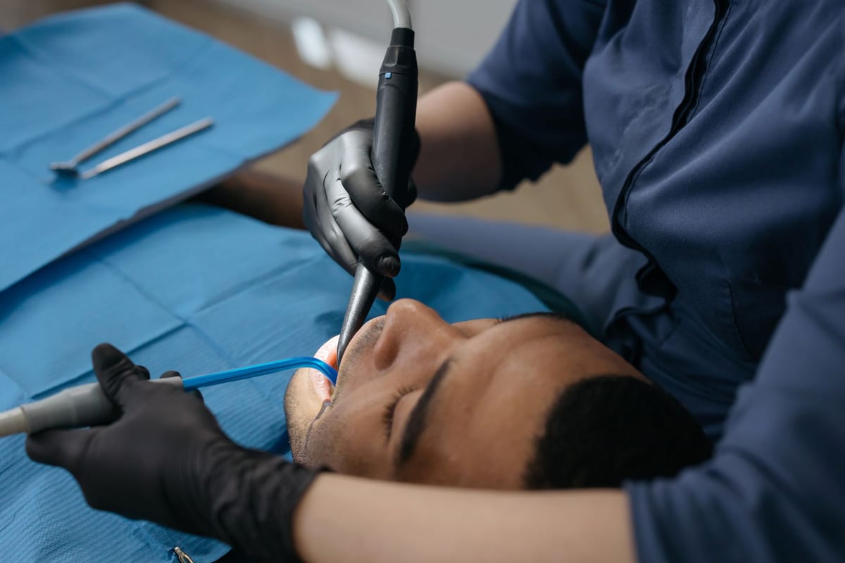 A dentist working on a patient's tooth with a handpiece and suction