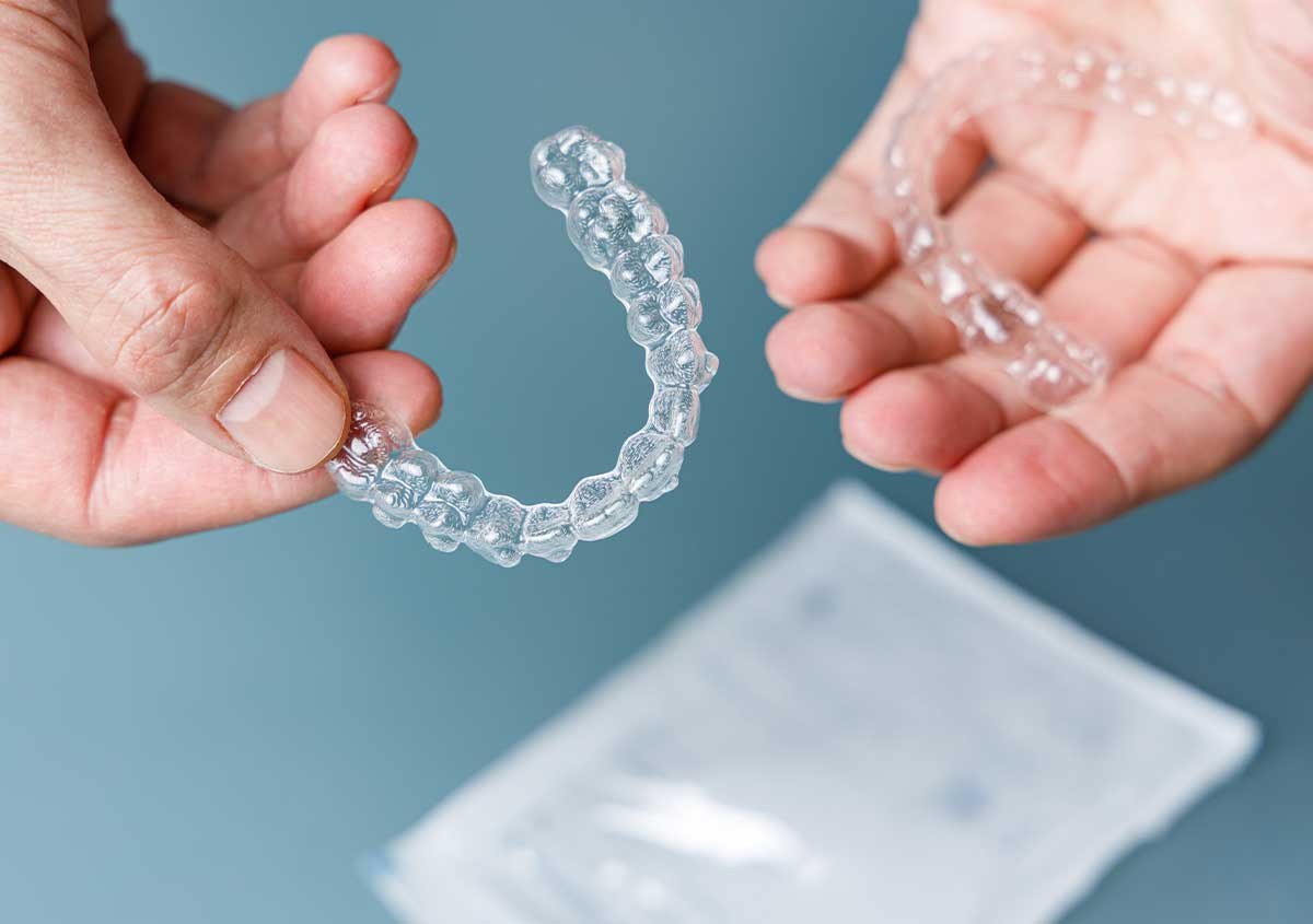 A pair of clear aligners held in two hands beside their case